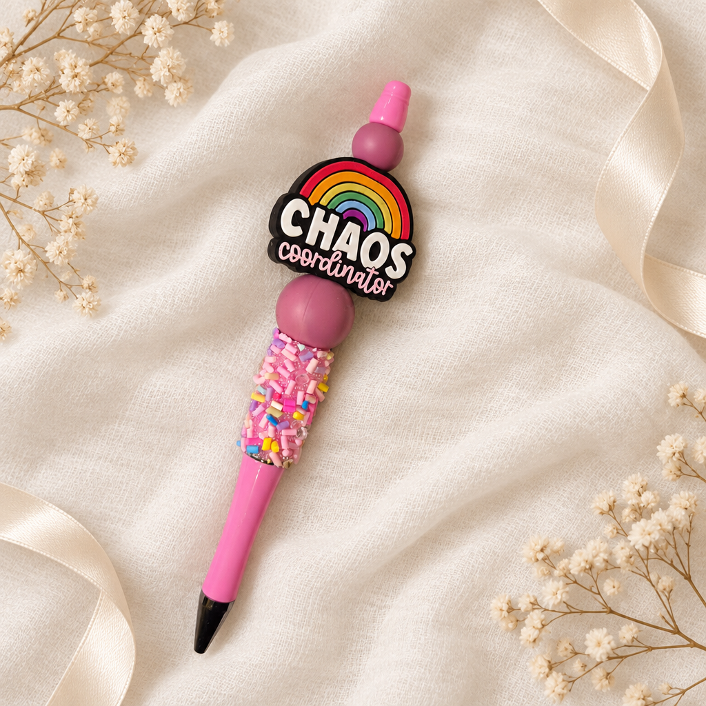 Pinker Kugelschreiber Chaos Coordinator mit Regenbogenmotiv, beerfarbenen Perlen und Zuckerstreusel-Optik auf weißem Musselin