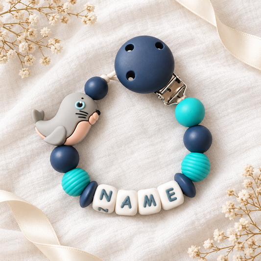 Personalisierte Schnullerkette mit Robbe, marineblauen und türkisen Perlen auf weißem Musselin