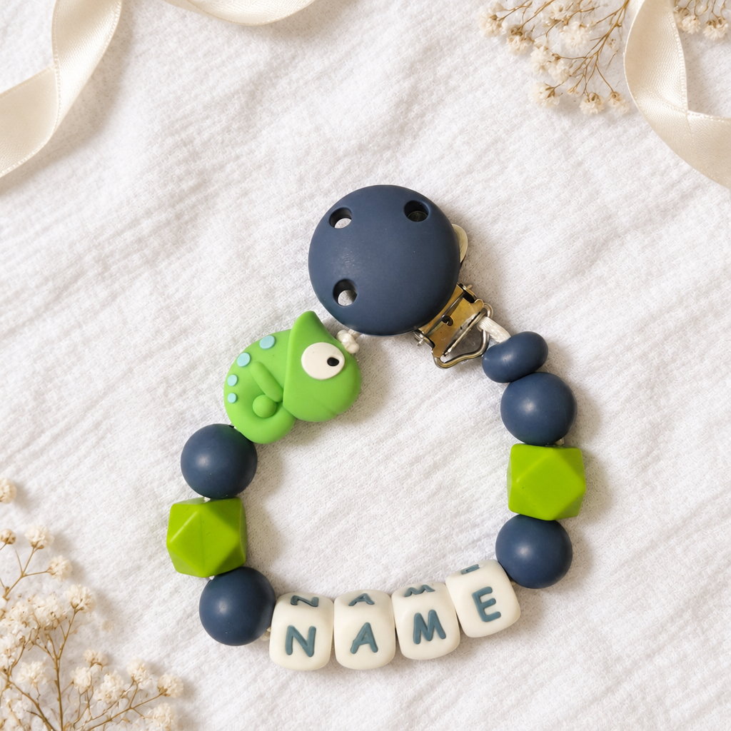 Personalisierbare Schnullerkette mit grünem Chamäleon und marineblauen Perlen auf weißem Musselin